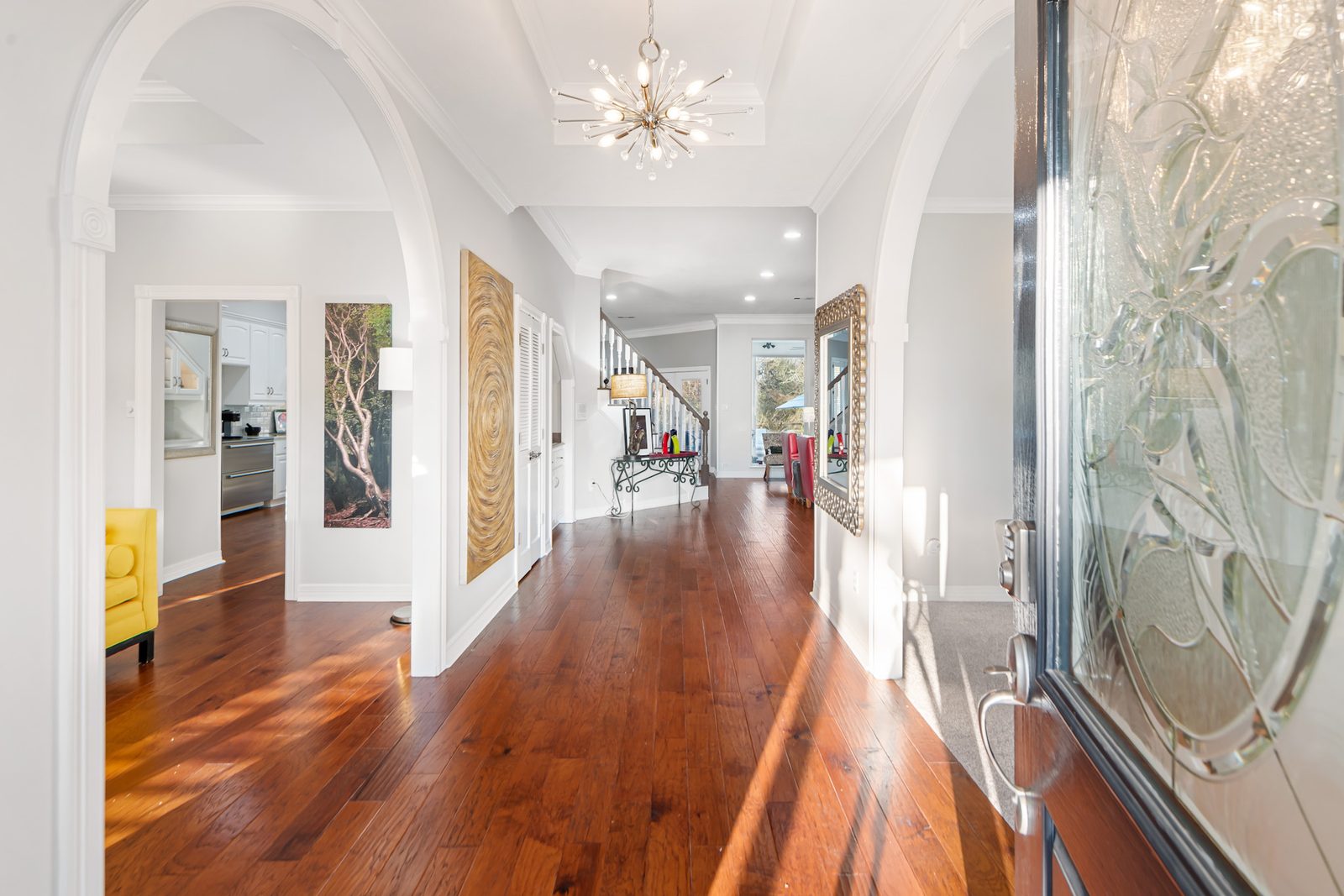 Arched entry hall with hardwood floors, art, and light from the front door