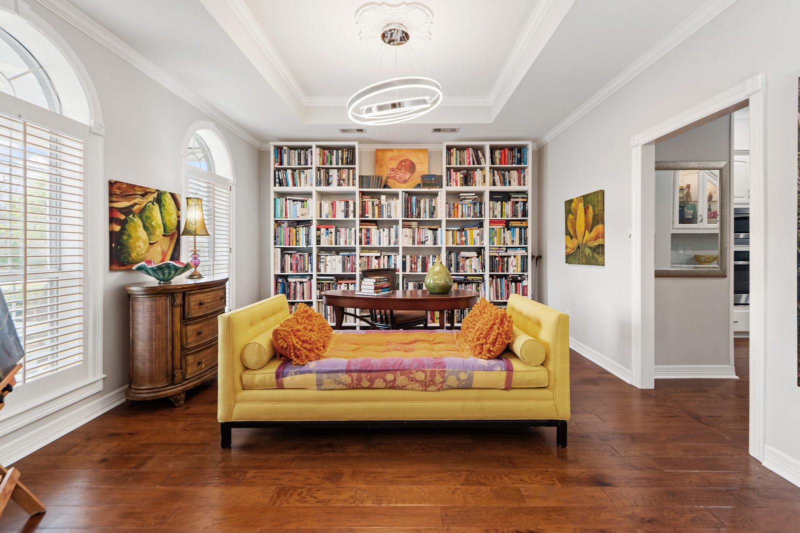 Library with a full wall of built-in bookshelves, a writing table, and a yellow daybed