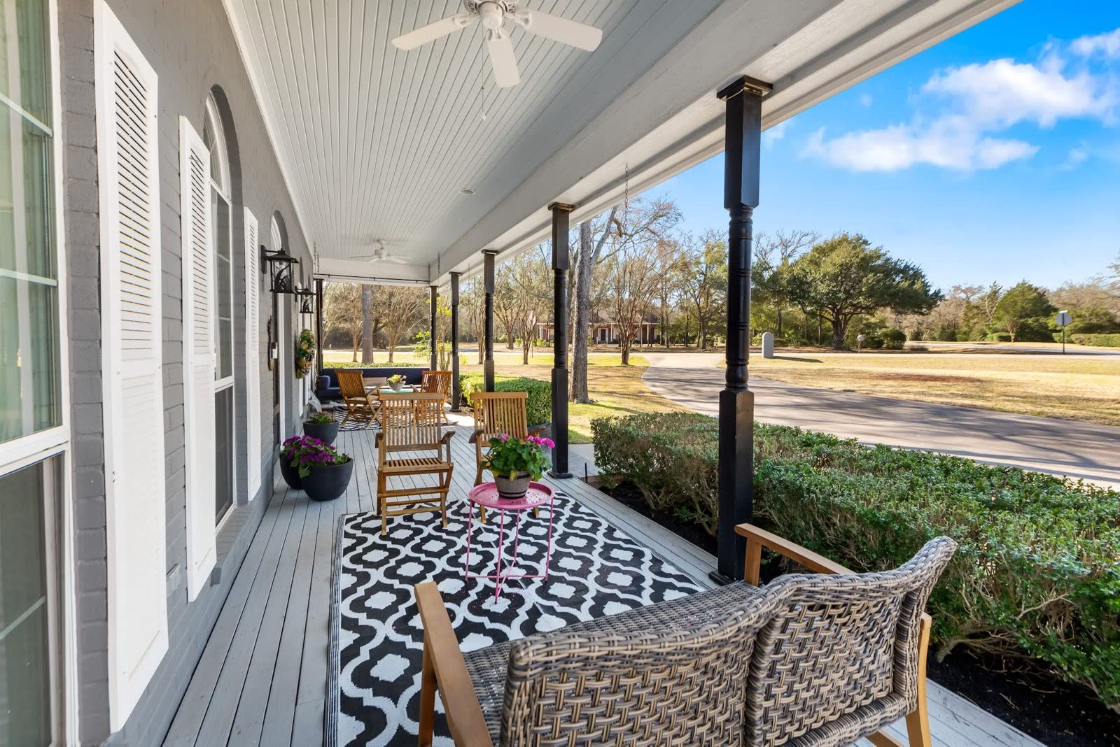 Full-length front porch with rocking chairs facing a quiet fenced estate lot